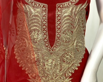 May include: A deep red tunic featuring intricate gold metallic embroidery around the neckline and chest area. The garment is made of a semi-sheer fabric and includes a matching red sheer dupatta draped to the side, with a tag labeled Angad Creations.