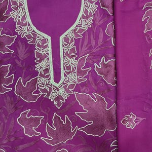 May include: A vibrant magenta fabric piece featuring intricate tone-on-tone embroidery of large, stylized leaves. The neckline is highlighted with a light mint green border, and the entire surface is covered in detailed, dark magenta leaf patterns.