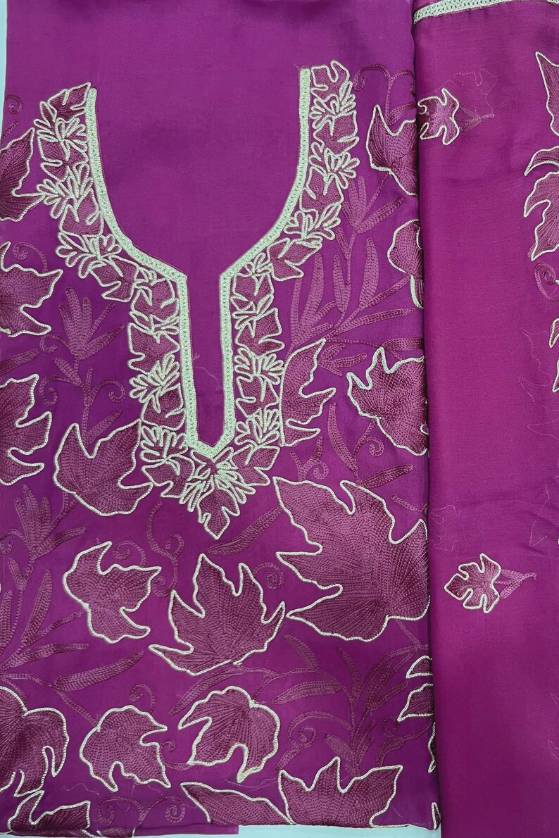 May include: A vibrant magenta fabric piece featuring intricate tone-on-tone embroidery of large, stylized leaves. The neckline is highlighted with a light mint green border, and the entire surface is covered in detailed, dark magenta leaf patterns.