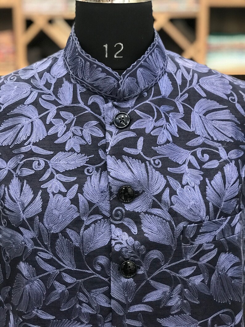 Pu&ograve; includere: Un gilet blu scuro con un motivo di ricamo floreale in una tonalit&agrave; di blu pi&ugrave; chiara. Il gilet ha un colletto alla coreana e tre bottoni.