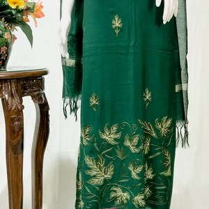 May include: A dark green dress with a leaf pattern embroidered on the bottom hem. The dress is made of a soft, flowing fabric and has a simple, elegant design.