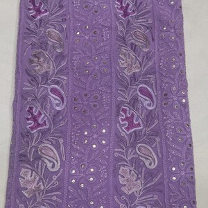May include: A lavender fabric featuring vertical panels of intricate embroidery. The design includes repeating paisley motifs, floral patterns, and leaf shapes in shades of purple, accented with small, reflective circular sequins throughout.