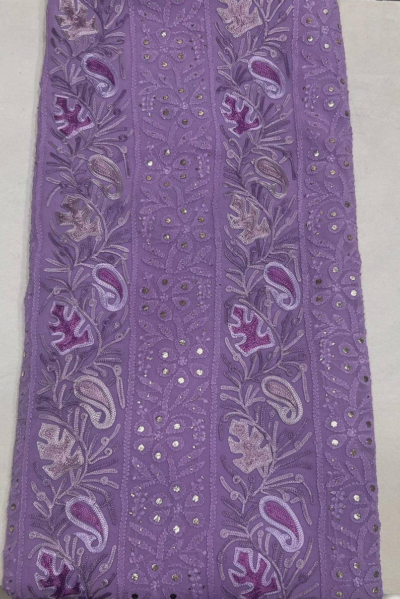 May include: A lavender fabric featuring vertical panels of intricate embroidery. The design includes repeating paisley motifs, floral patterns, and leaf shapes in shades of purple, accented with small, reflective circular sequins throughout.