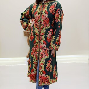 May include: A long, dark green coat with intricate floral embroidery in shades of red, orange, and yellow. The coat has a button closure and long sleeves.