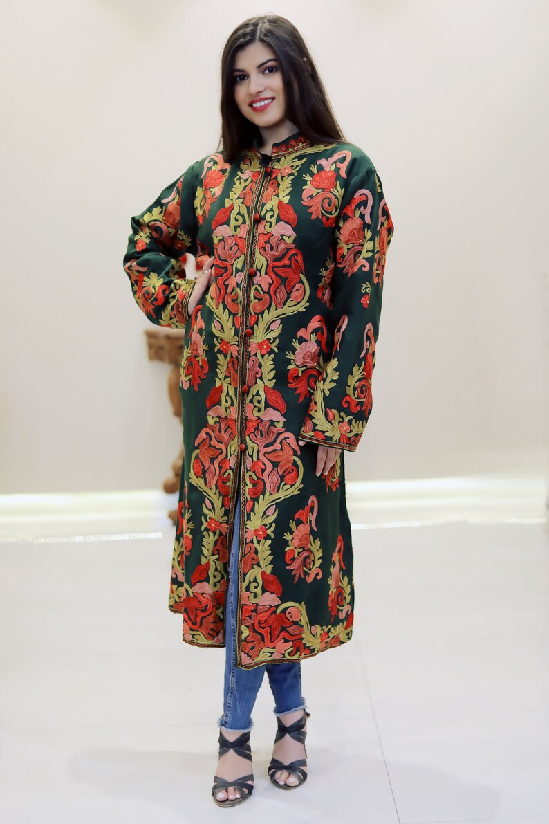 May include: A long, dark green coat with intricate floral embroidery in shades of red, orange, and yellow. The coat has a button closure and long sleeves.