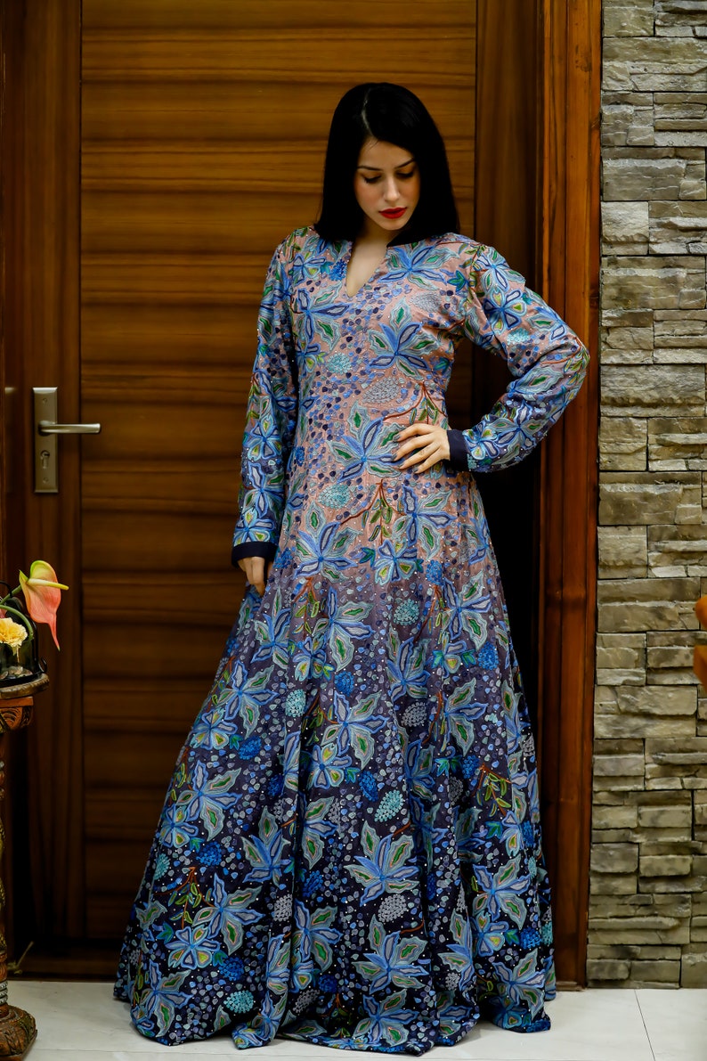May include: A long, flowing dress with a floral print in shades of blue, pink, and green. The dress has a V-neckline and long sleeves.