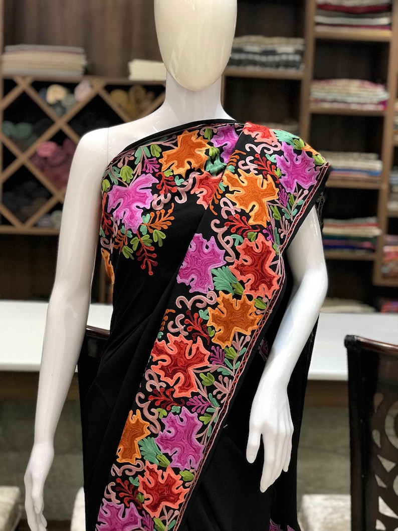 Peut inclure: Sari noir avec des motifs floraux brod&eacute;s color&eacute;s. La broderie pr&eacute;sente une vari&eacute;t&eacute; de couleurs, notamment le rose, l'orange, le vert et le rouge.