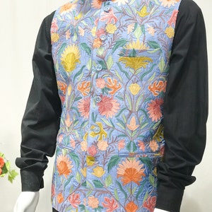 May include: A light blue vest with a floral pattern embroidered in shades of pink, yellow, orange, and green. The vest has a mandarin collar and a button closure.