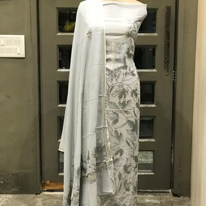 Op de afbeelding: Een grijze en witte geborduurde jurk met een bloemenpatroon. De jurk is op een mannequin en heeft een bijpassende dupatta.