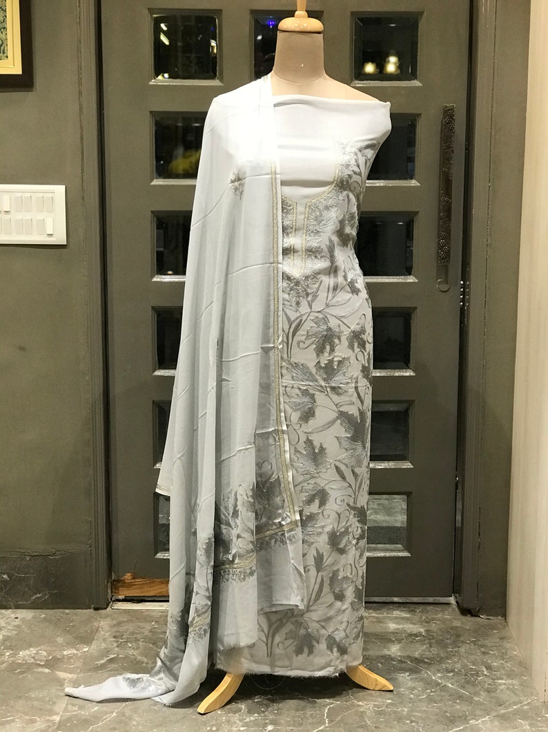 Op de afbeelding: Een grijze en witte geborduurde jurk met een bloemenpatroon. De jurk is op een mannequin en heeft een bijpassende dupatta.