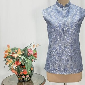 Puede incluir: Un chaleco sin mangas de color azul claro con un estampado floral blanco. El chaleco tiene un cuello mandar&iacute;n y cierre de botones. Se muestra en un maniqu&iacute;.