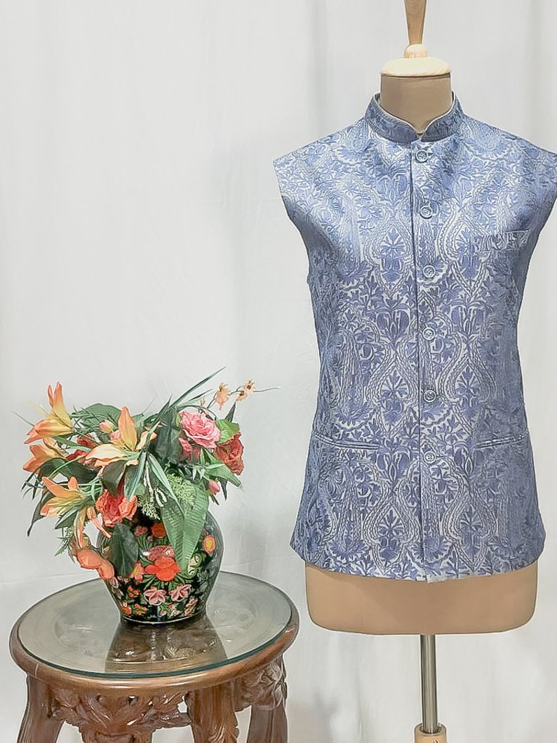 Puede incluir: Un chaleco sin mangas de color azul claro con un estampado floral blanco. El chaleco tiene un cuello mandar&iacute;n y cierre de botones. Se muestra en un maniqu&iacute;.