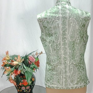 Puede incluir: Un chaleco verde sin mangas con un estampado paisley blanco. El chaleco est&aacute; en un maniqu&iacute; blanco.