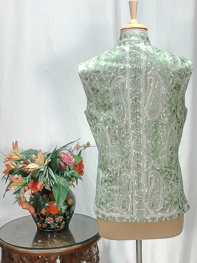 Puede incluir: Un chaleco verde sin mangas con un estampado paisley blanco. El chaleco est&aacute; en un maniqu&iacute; blanco.