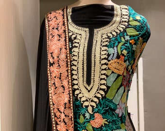 May include: A black embroidered dress with a floral pattern in shades of green, blue, pink, and orange. The dress has a V-neckline and a long sleeve. The fabric is sheer and the embroidery is intricate.