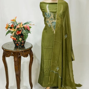 May include: A green dress with a floral embroidery design. The dress is on a mannequin and has a matching dupatta.