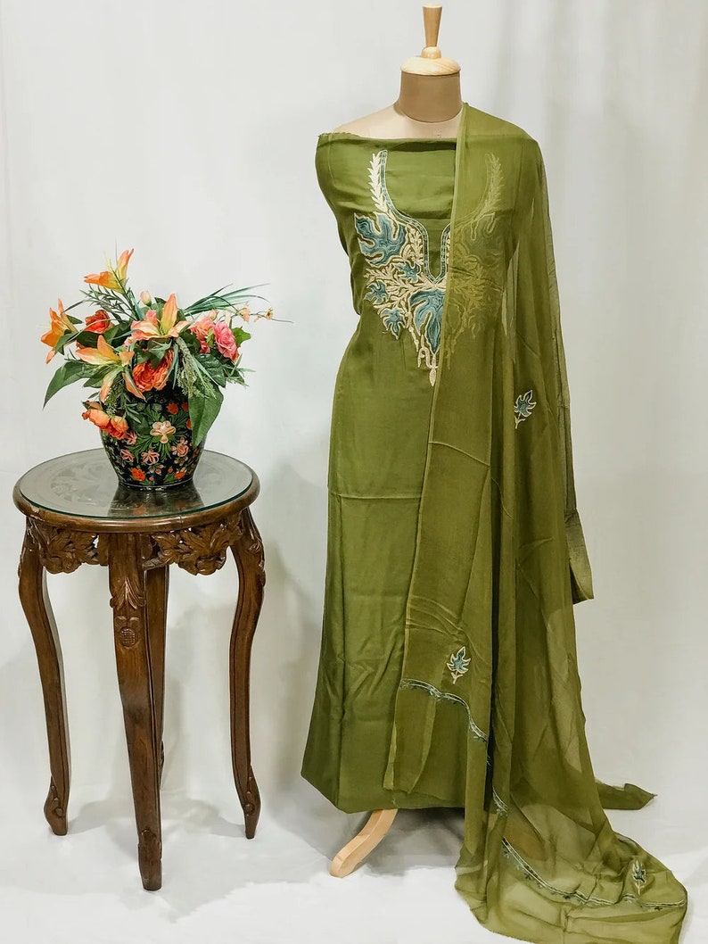 May include: A green dress with a floral embroidery design. The dress is on a mannequin and has a matching dupatta.