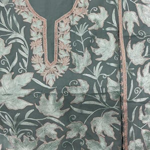 May include: A sage green tunic featuring intricate embroidery of light green maple leaves with soft pink outlines. The garment has a keyhole neckline bordered by matching pink and green floral stitching, with a coordinating fabric panel to the side.