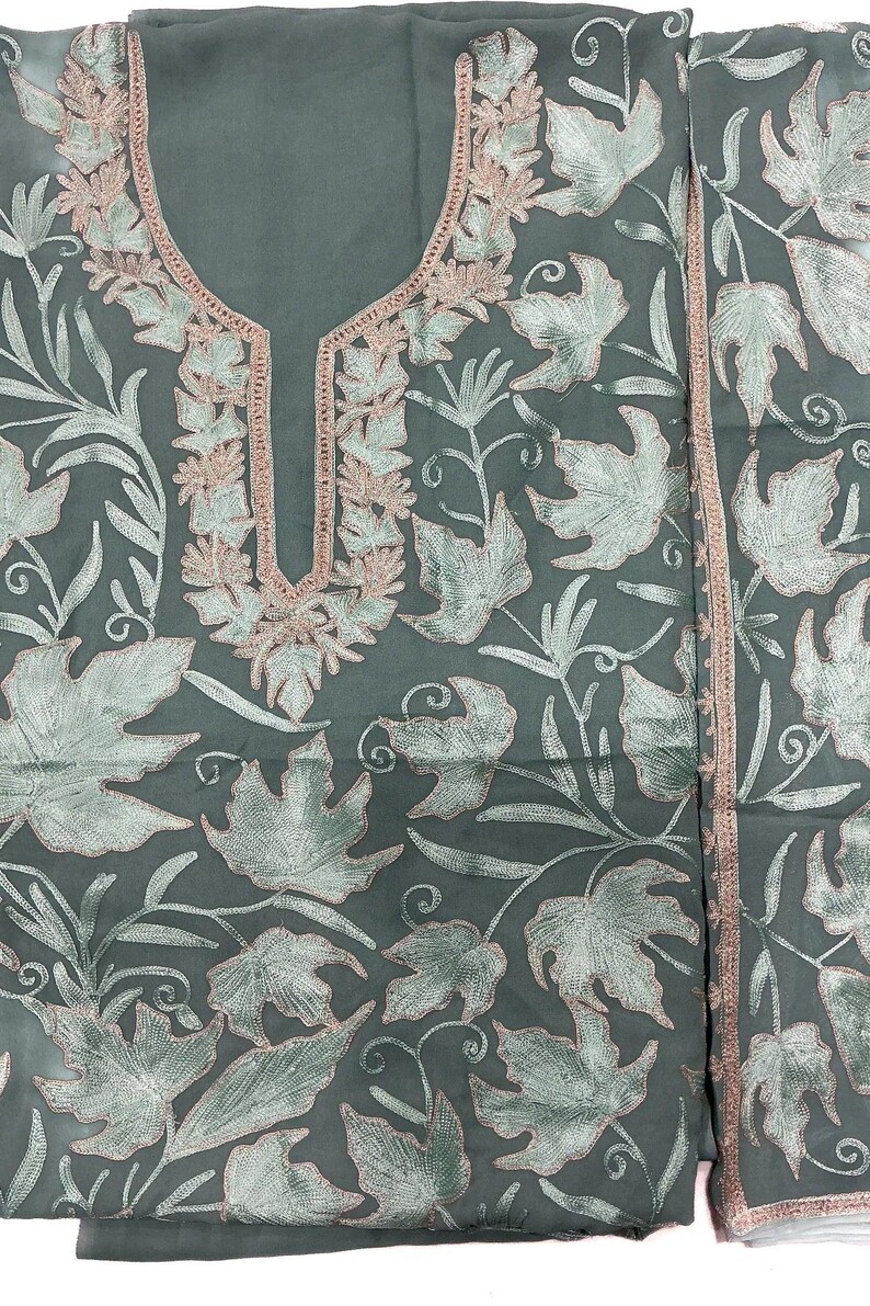 May include: A sage green tunic featuring intricate embroidery of light green maple leaves with soft pink outlines. The garment has a keyhole neckline bordered by matching pink and green floral stitching, with a coordinating fabric panel to the side.