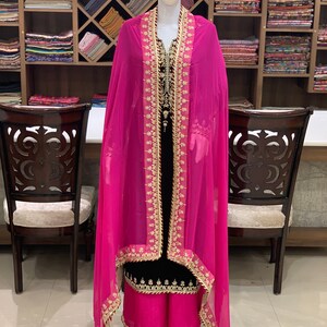 May include: A black and pink salwar kameez with gold embroidery. The kameez has a long, flowing design and the salwar is a loose-fitting trouser. The dupatta is a long, sheer scarf.