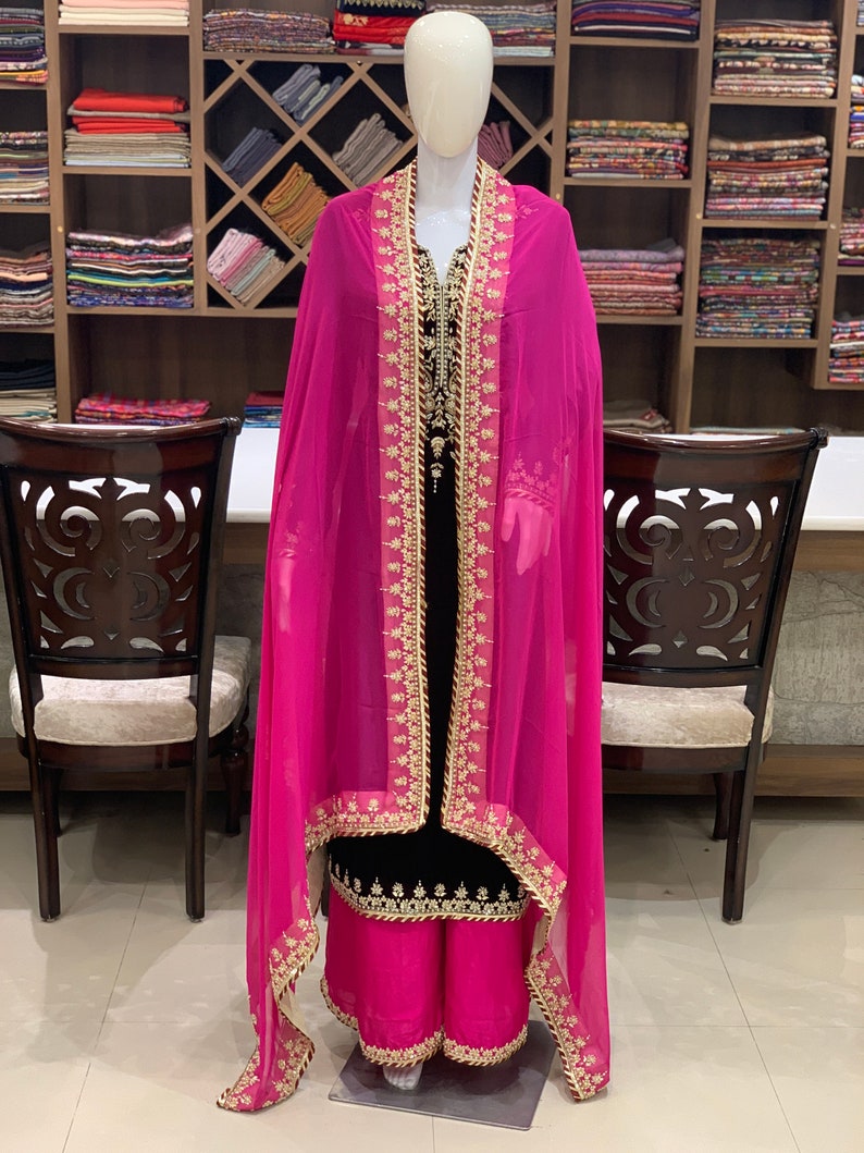 May include: A black and pink salwar kameez with gold embroidery. The kameez has a long, flowing design and the salwar is a loose-fitting trouser. The dupatta is a long, sheer scarf.