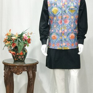 May include: A blue waistcoat with a floral pattern, worn over a black shirt and white pants. The waistcoat has a mandarin collar and a button closure.