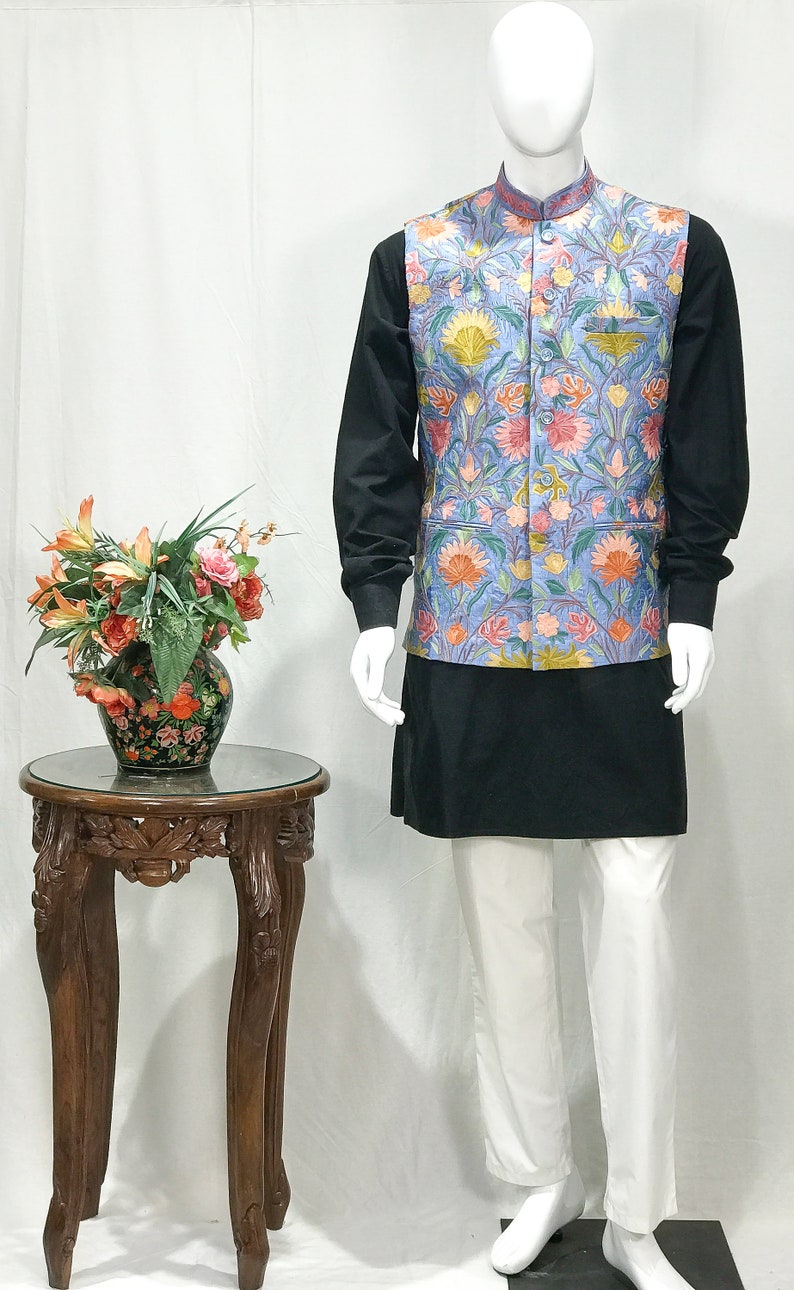 May include: A blue waistcoat with a floral pattern, worn over a black shirt and white pants. The waistcoat has a mandarin collar and a button closure.