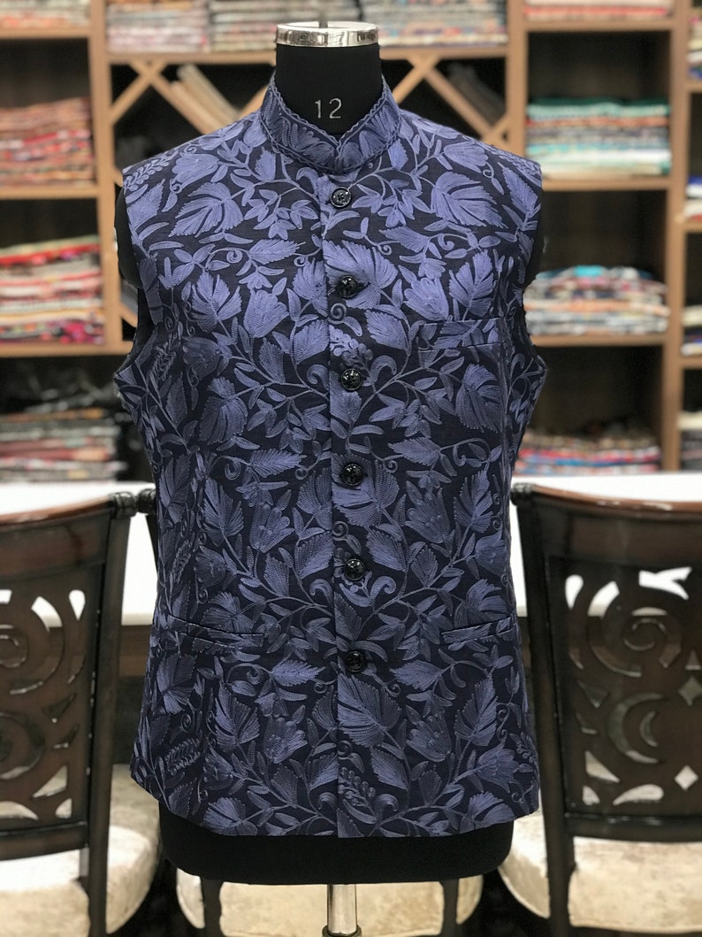 Pu&ograve; includere: Un gilet blu navy senza maniche con un motivo floreale. Il gilet ha un colletto alla coreana e una chiusura con bottoni.