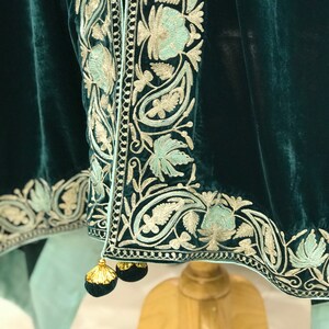 May include: A teal velvet shawl with a delicate floral embroidery pattern in silver and light blue. The shawl has a fringe trim and tassels.