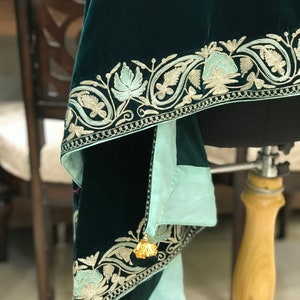 May include: A dark green velvet shawl with a light blue lining and intricate gold embroidery. The shawl has a tassel on one corner.