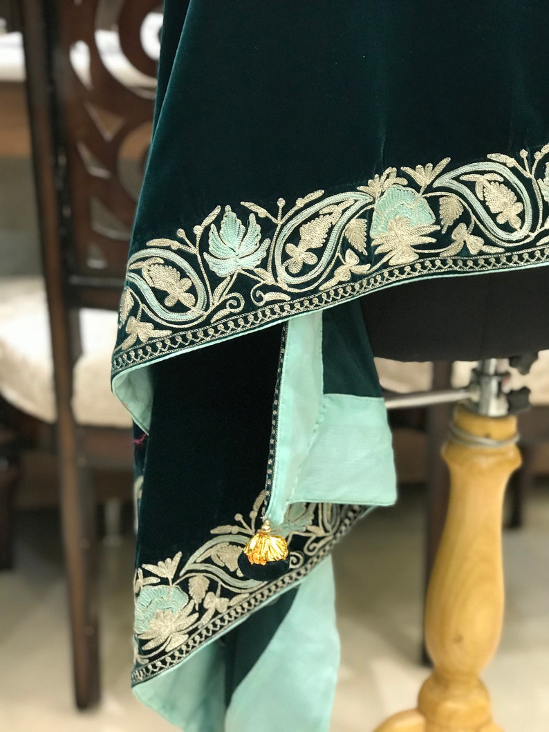 May include: A dark green velvet shawl with a light blue lining and intricate gold embroidery. The shawl has a tassel on one corner.