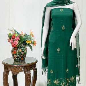 May include: A green cotton dress with gold leaf embroidery. The dress is on a white mannequin and has a matching green dupatta with gold trim.