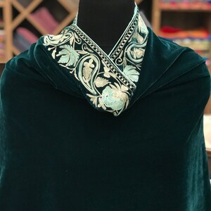 May include: A dark green velvet shawl with a white and light blue embroidered border. The border features a floral design.