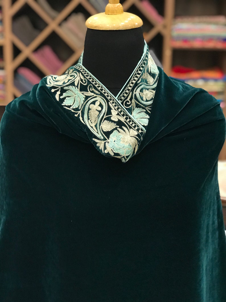 May include: A dark green velvet shawl with a white and light blue embroidered border. The border features a floral design.