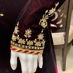 May include: A maroon velvet garment with gold and pearl embroidery on the sleeve. The sleeve has a maroon, gold, and white trim.