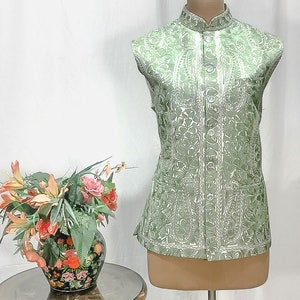 Puede incluir: Un chaleco verde sin mangas con un estampado floral blanco y un cuello mandar&iacute;n. El chaleco tiene cierre de bot&oacute;n y dos bolsillos.