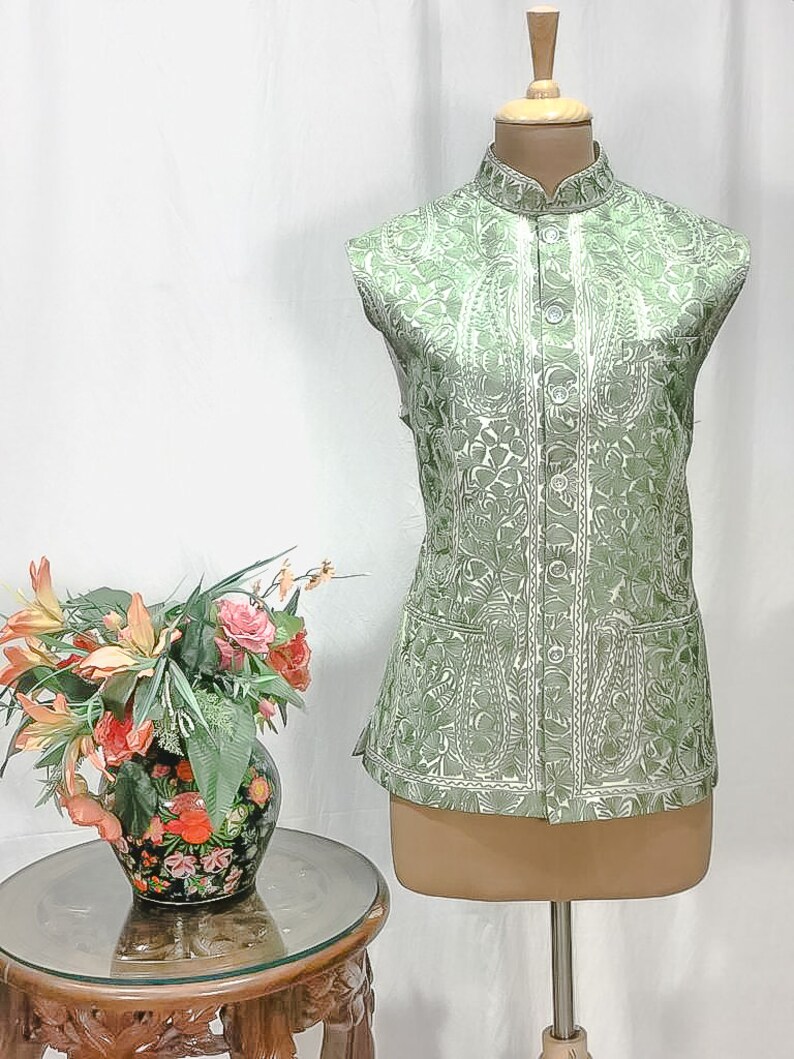 Puede incluir: Un chaleco verde sin mangas con un estampado floral blanco y un cuello mandar&iacute;n. El chaleco tiene cierre de bot&oacute;n y dos bolsillos.