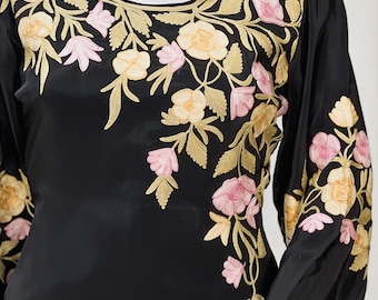 May include: Black long-sleeved dress with a floral embroidery design in pink, yellow, and gold thread. The embroidery is on the neckline and the sleeves.