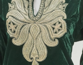 Può includere: Una tunica in velluto verde scuro con un collo ricamato in oro. Il ricamo presenta un motivo floreale con dettagli intricati.