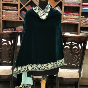 May include: A dark green velvet shawl with a light green and white embroidered border. The shawl is draped over a mannequin and has a light green lining.