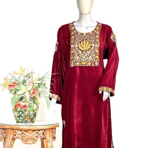 May include: A long-sleeved, deep maroon velvet tunic featuring a prominent rectangular chest panel with intricate gold and pink floral embroidery. The garment includes matching embroidered trim along the cuffs and the lower hemline.
