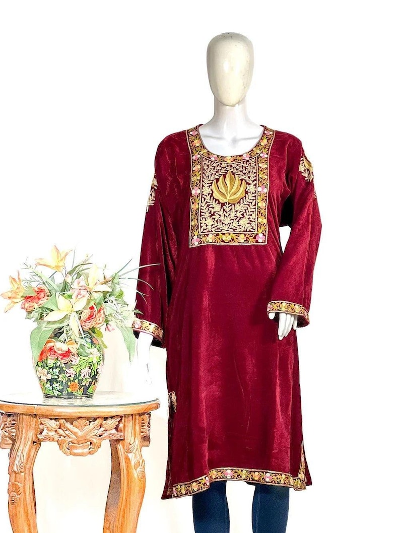 May include: A long-sleeved, deep maroon velvet tunic featuring a prominent rectangular chest panel with intricate gold and pink floral embroidery. The garment includes matching embroidered trim along the cuffs and the lower hemline.
