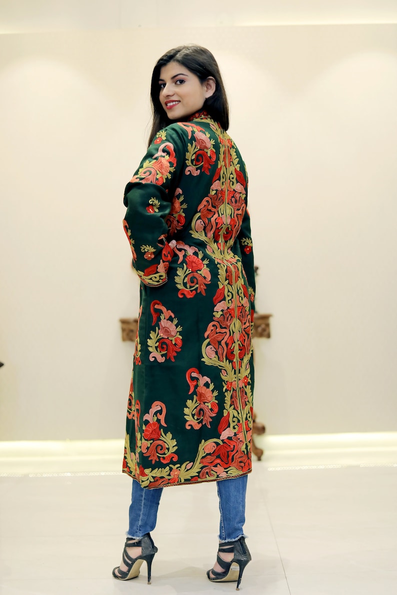 May include: A long, dark green embroidered coat with a floral pattern in shades of red, pink, and yellow. The coat has a high neckline and long sleeves.