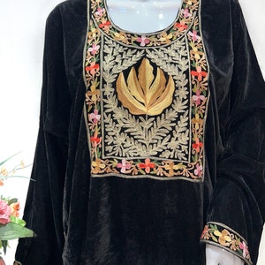 May include: A black velvet tunic featuring a prominent rectangular chest panel with gold thread embroidery of a central leaf motif surrounded by intricate floral patterns in pink, orange, and yellow. The sleeves have matching floral embroidery.
