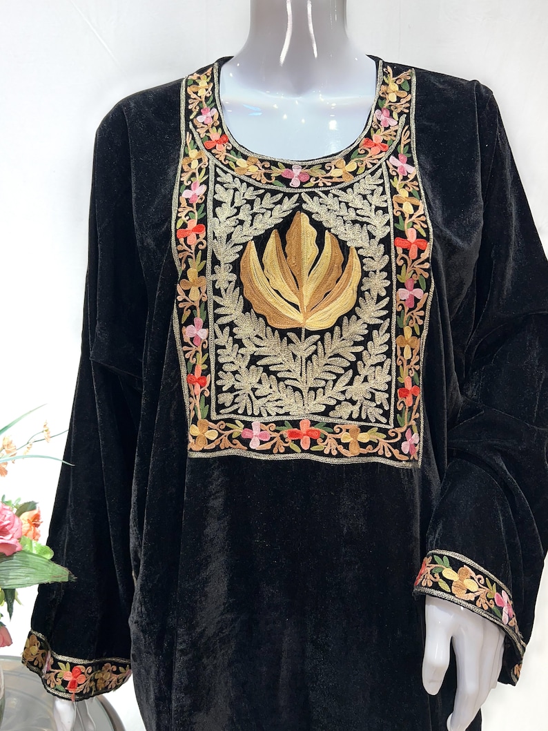 May include: A black velvet tunic featuring a prominent rectangular chest panel with gold thread embroidery of a central leaf motif surrounded by intricate floral patterns in pink, orange, and yellow. The sleeves have matching floral embroidery.