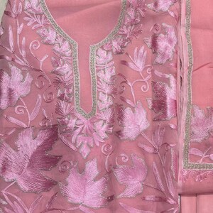 May include: A light pink sheer fabric garment featuring intricate tonal pink embroidery of large leaves and swirling vines. The neckline is framed with a metallic silver border, and the design includes a matching pink fabric panel with a silver edge.