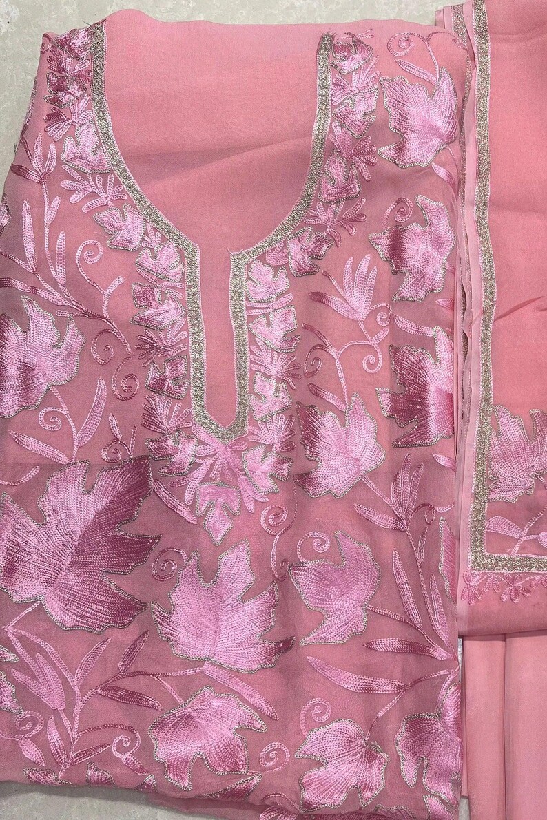 May include: A light pink sheer fabric garment featuring intricate tonal pink embroidery of large leaves and swirling vines. The neckline is framed with a metallic silver border, and the design includes a matching pink fabric panel with a silver edge.