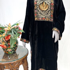 May include: A black velvet tunic featuring a prominent rectangular chest panel with gold leaf embroidery and intricate floral borders in pink, orange, and green. The long-sleeved garment includes matching floral embroidery along the cuffs and hemline.
