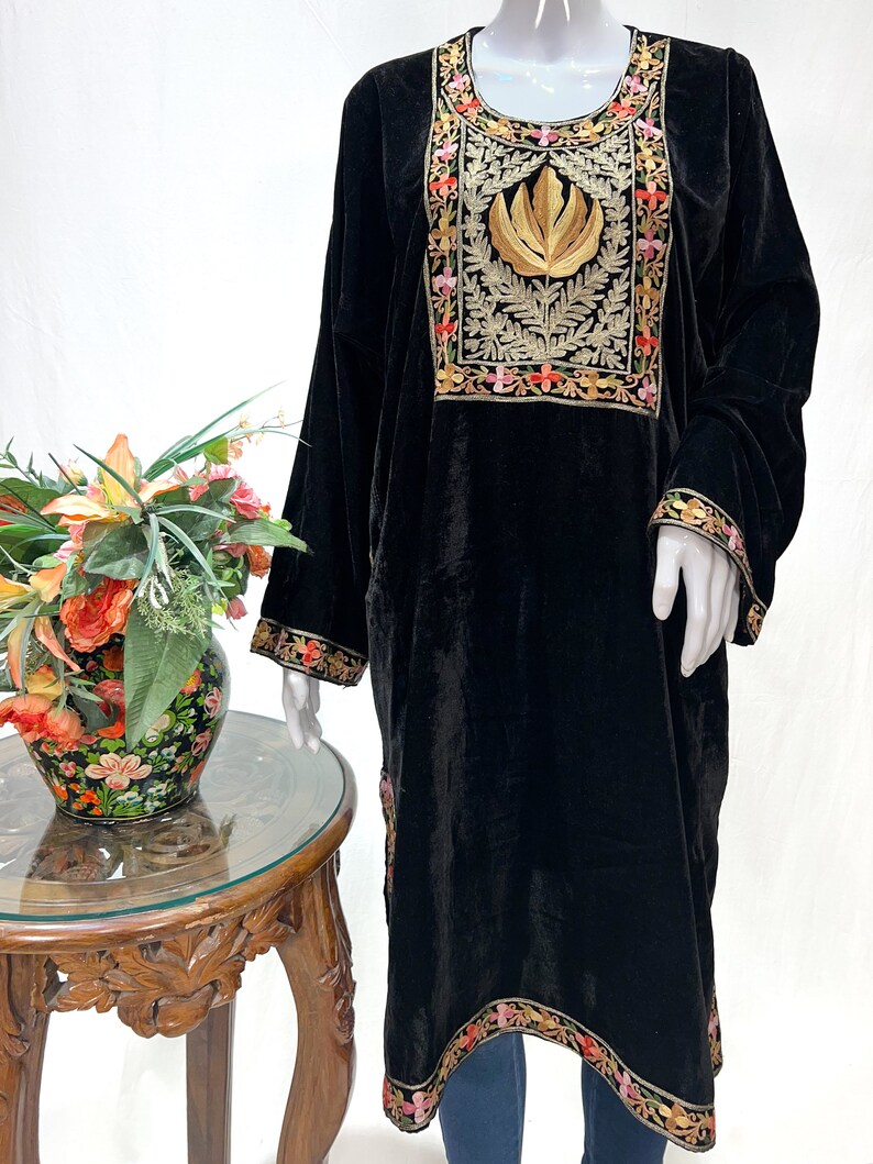 May include: A black velvet tunic featuring a prominent rectangular chest panel with gold leaf embroidery and intricate floral borders in pink, orange, and green. The long-sleeved garment includes matching floral embroidery along the cuffs and hemline.