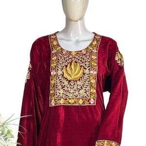 May include: A deep maroon velvet tunic featuring a prominent rectangular chest panel with intricate gold thread embroidery depicting a central lotus motif surrounded by floral patterns in pink, yellow, and green. The long sleeves have matching trim.